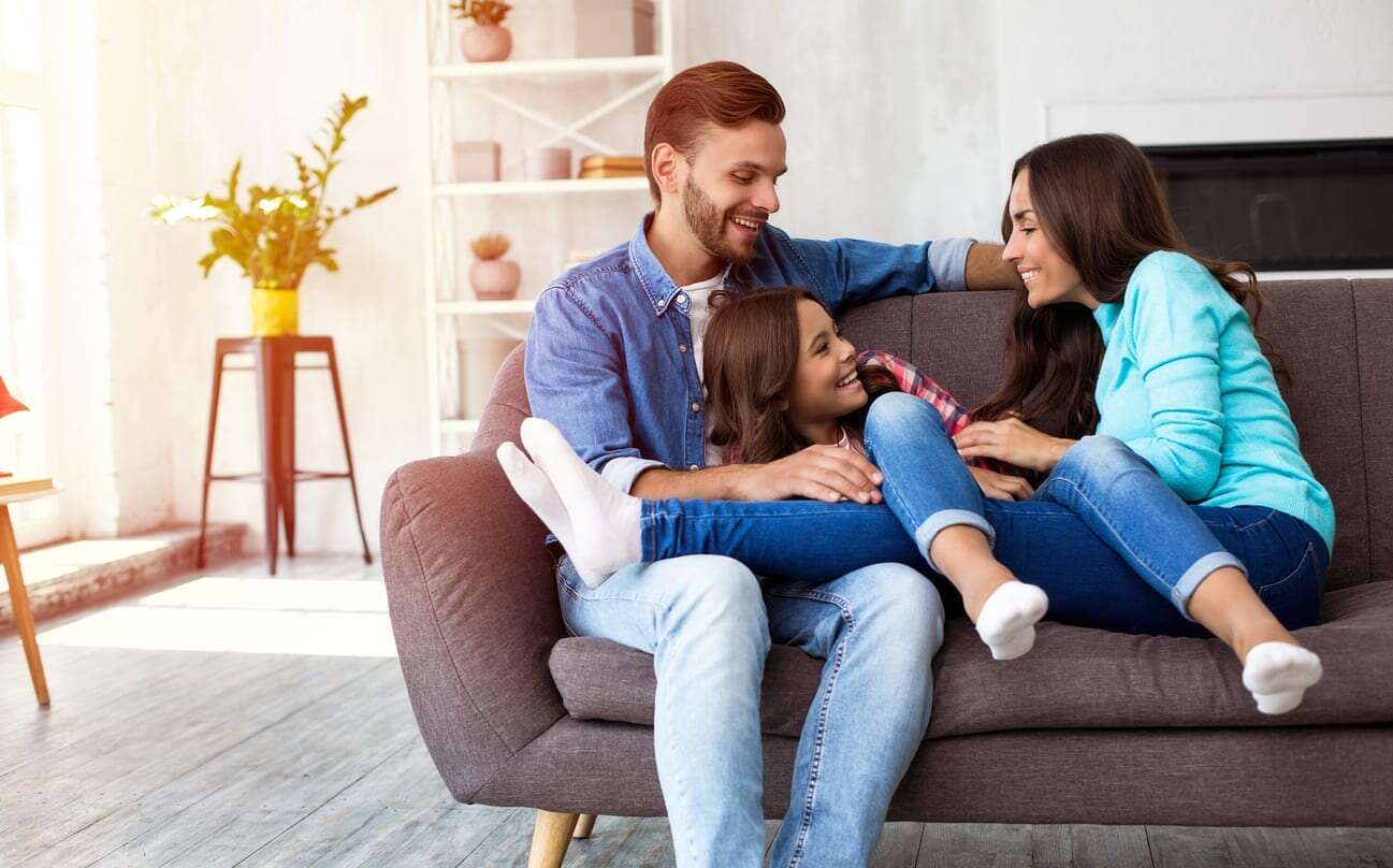 Family of three smiling on couch in their home.